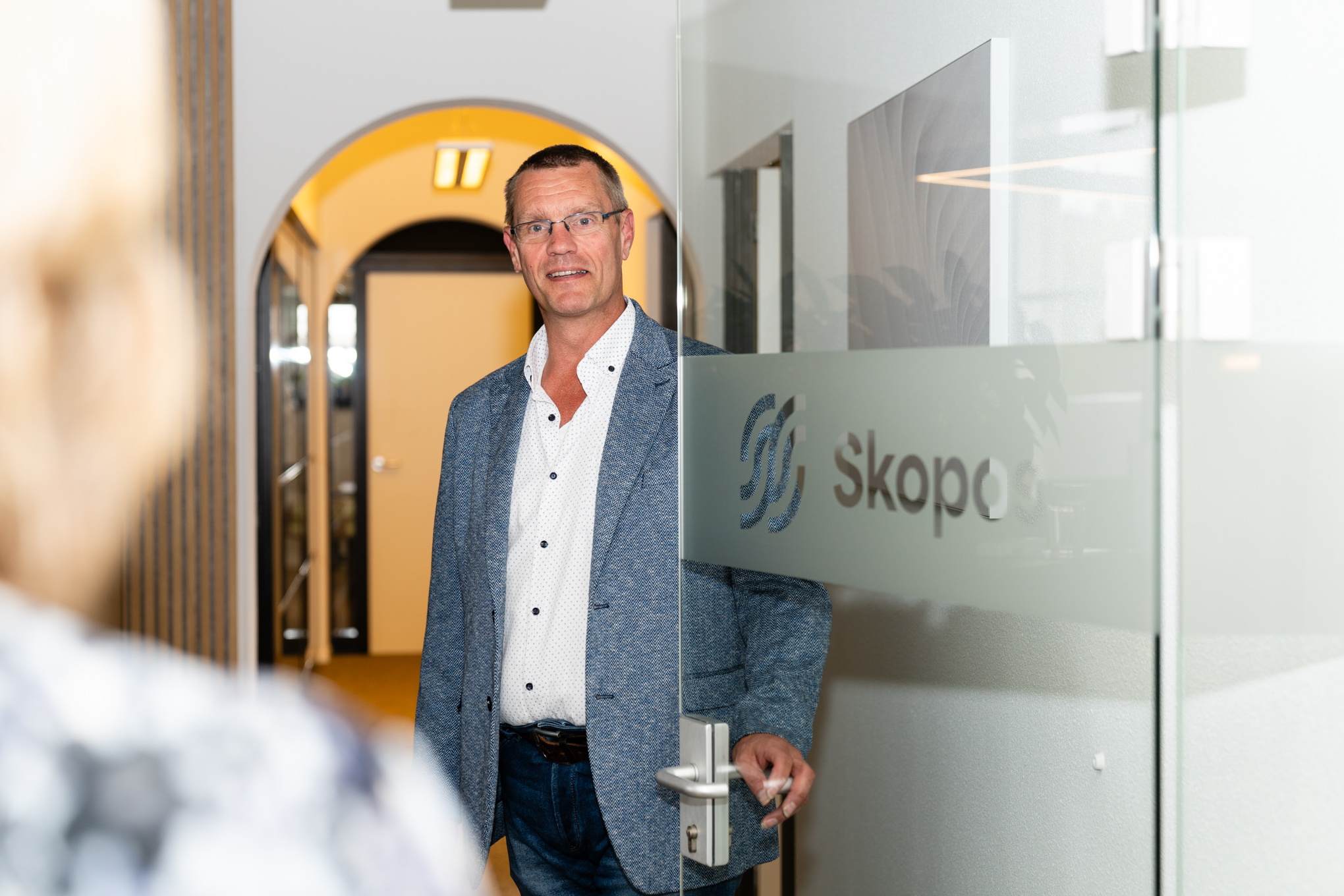 Skopos-consultant opent de glazen deur met het Skopos-logo voor een kennismaking